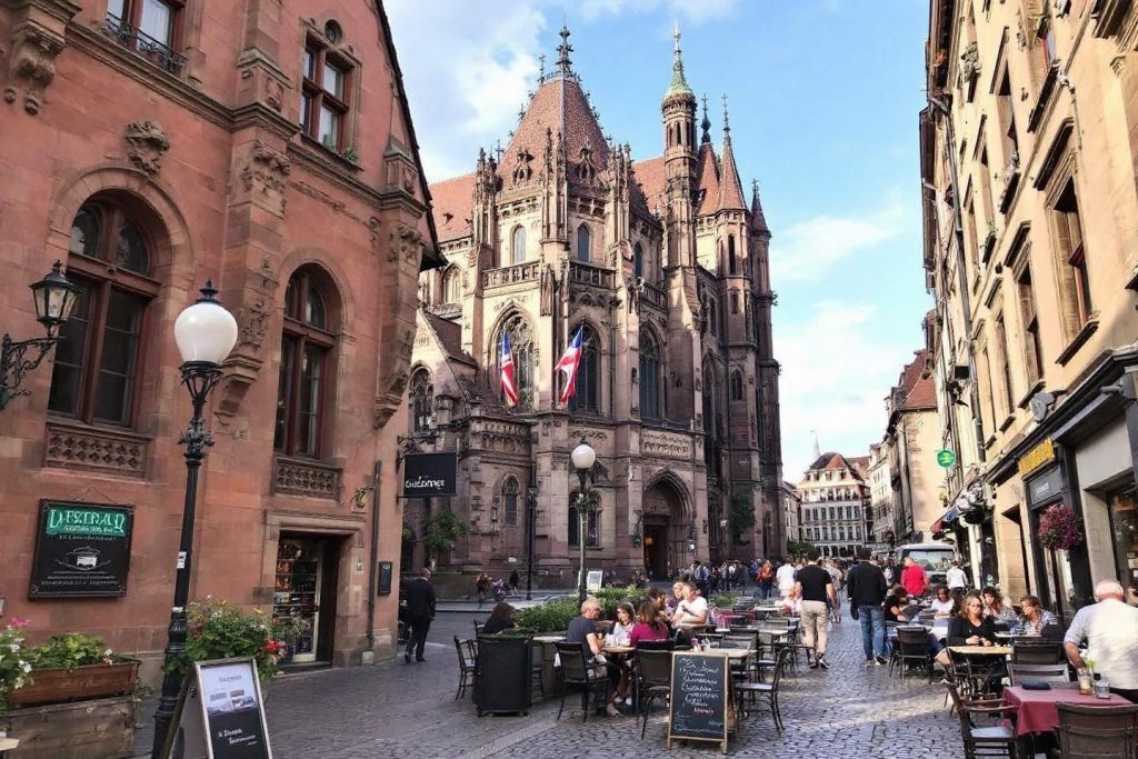 Église médiévale au cœur d'une rue pavée avec terrasses