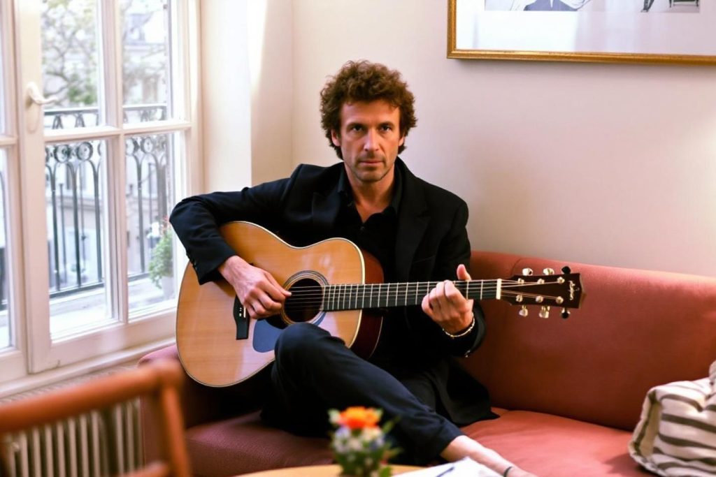 Homme aux cheveux bouclés jouant de la guitare sur un canapé