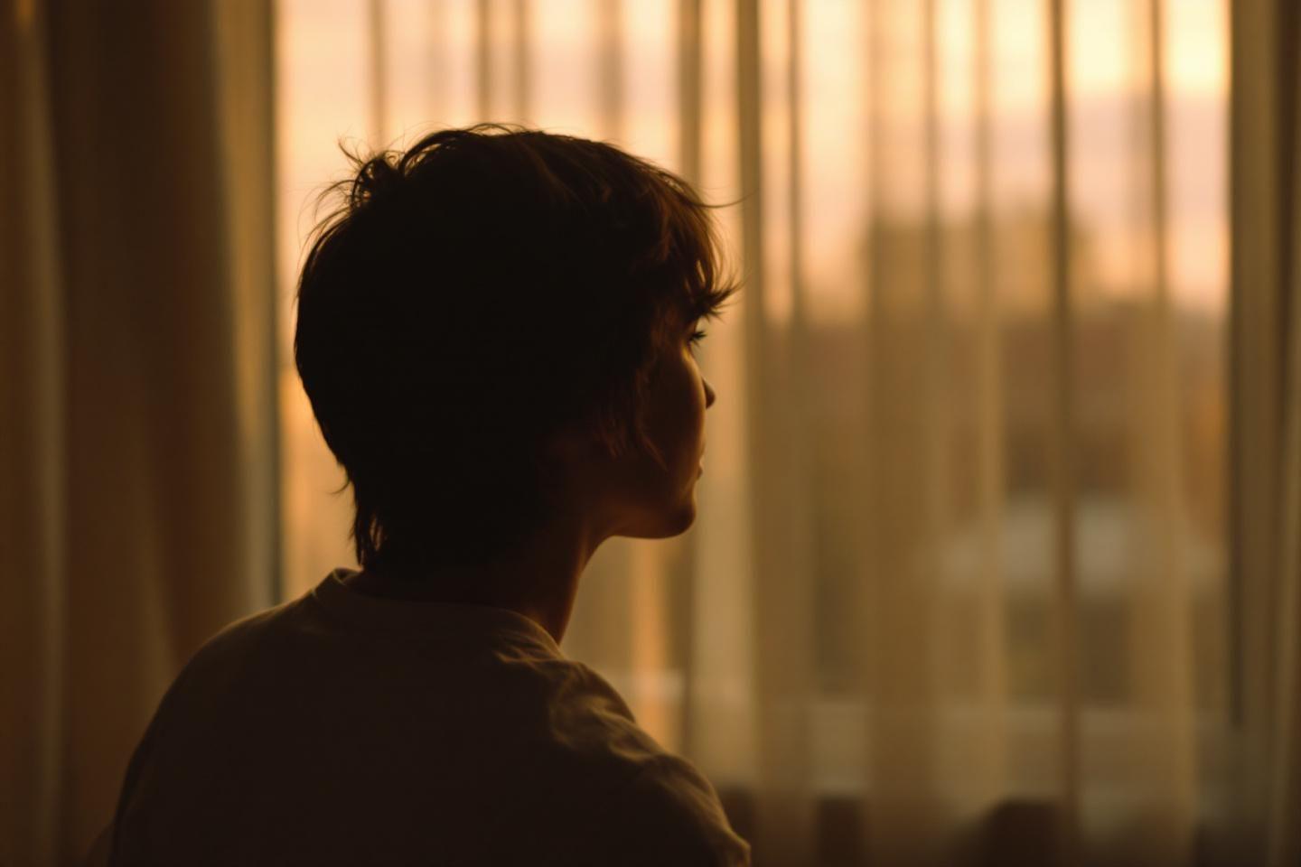 Profil sombre d'une personne regardant &agrave; travers les rideaux